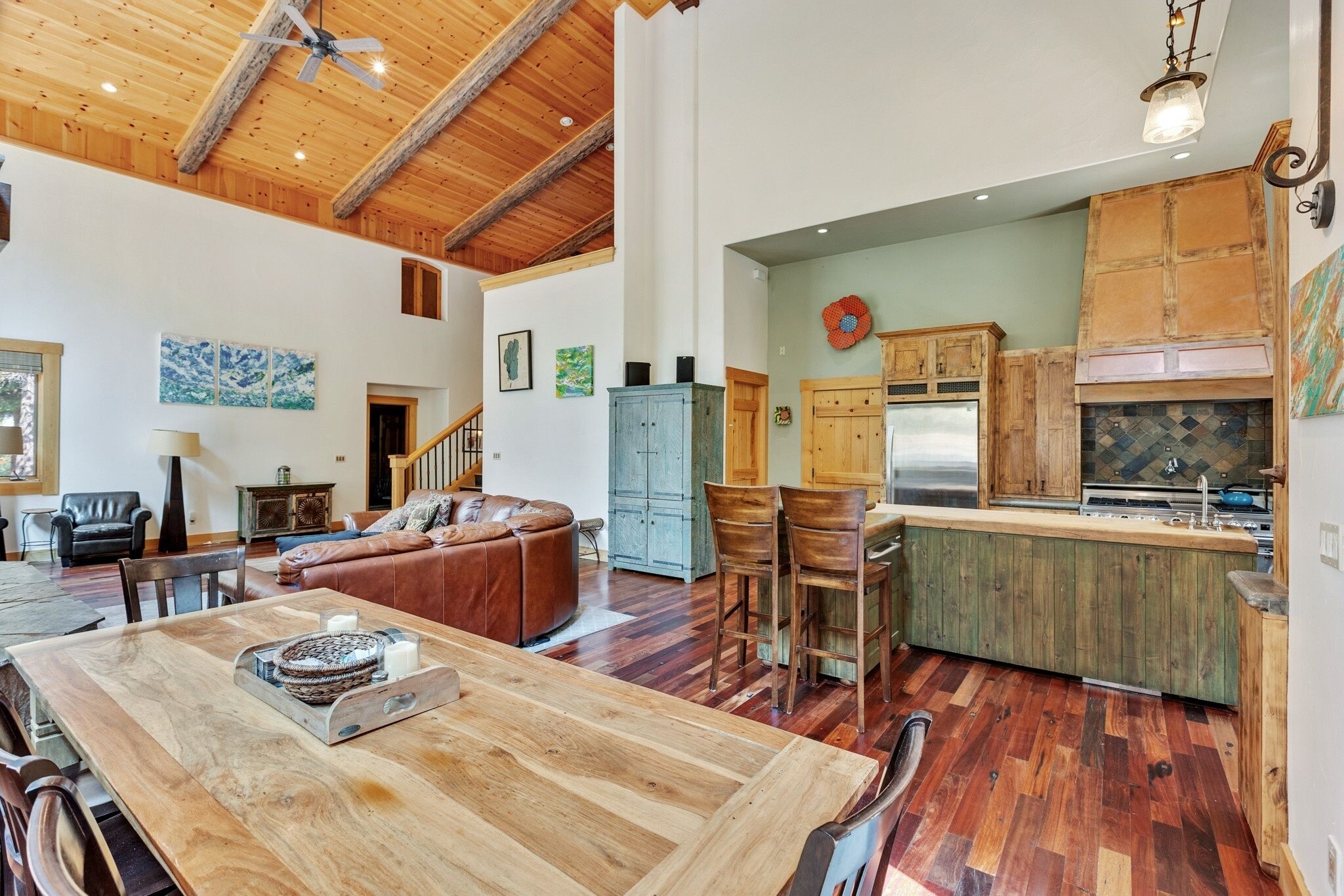 A spacious living area with a wooden dining table, a leather sofa, and a kitchen with wooden cabinets and a large island.