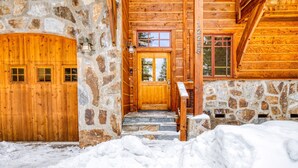 A wooden cabin with a stone exterior, a wooden door, and a stone staircase leading to a wooden deck.