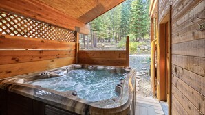 A wooden hot tub with a view of a forested area.