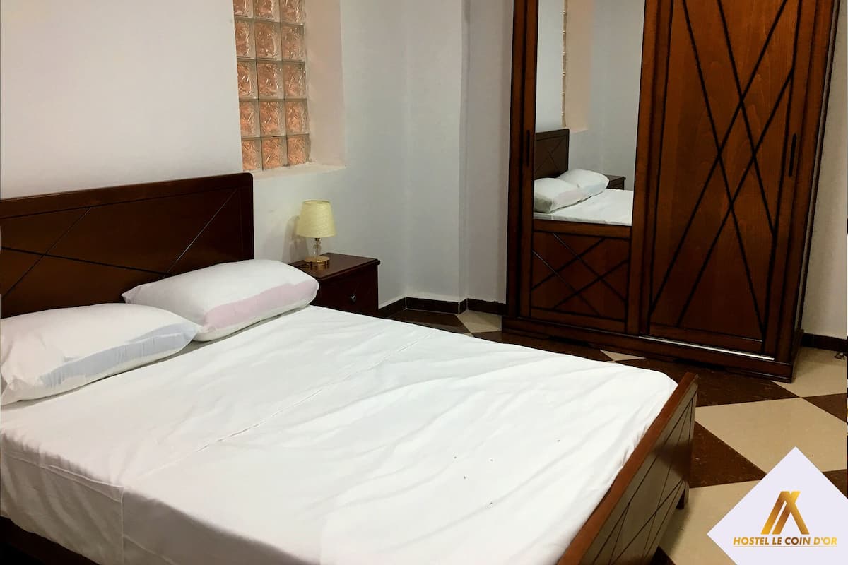 A hotel room with a bed, a nightstand with a lamp, a wooden wardrobe, and a mirror.