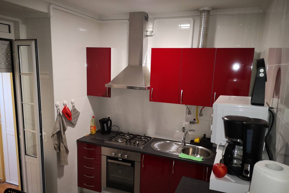 Uma cozinha compacta com armários vermelhos, fogão a gás, forno embutido, pia e cafeteira.