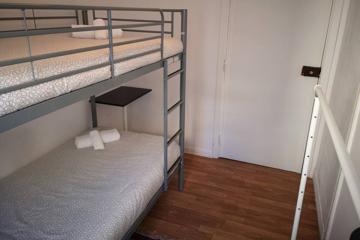 Quarto com beliche, piso de madeira e porta branca.