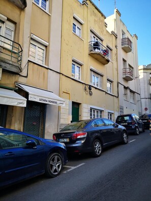 Vista de la calle con coches estacionados y un edificio con un cartel que dice 'LEITARIA MONDEGO'.