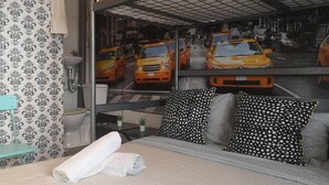 A hotel room with a bed, a bathroom, and a view of yellow taxis outside.