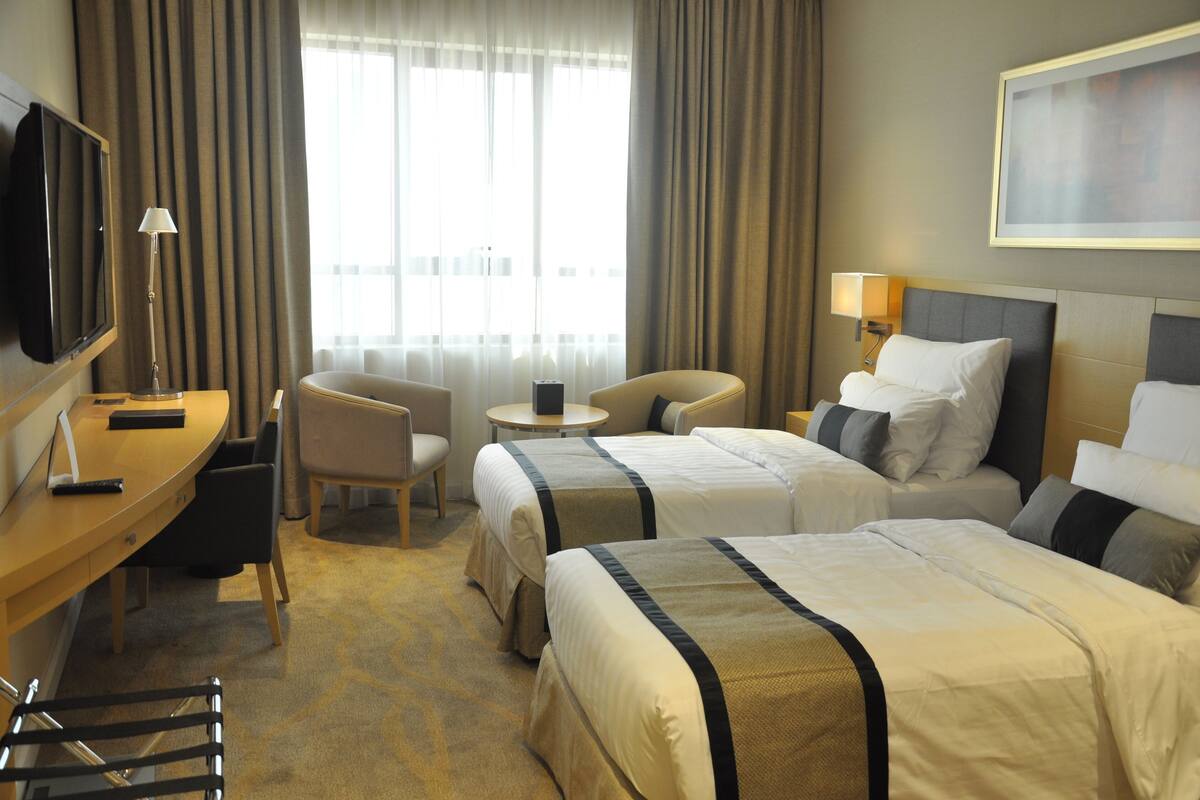 Habitación de hotel con dos camas, un escritorio, una silla, un televisor y una ventana con cortinas.