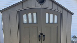 Ein großes, einstöckiges Gartenhaus mit geneigtem Dach und einem runden Lüftungseinsatz obenauf.