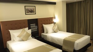 A hotel room with two beds, wooden flooring, a headboard with a light, and a framed picture on the wall. - Ocean Pearl Inn (Mangaluru)