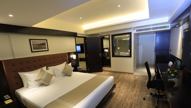 A hotel room with a large bed, a desk, a chair, and a TV. - Ocean Pearl Inn (Mangaluru)
