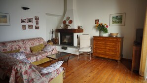 A living room with a sofa, a wooden floor, a fireplace, a white chair, a wooden dresser, and framed pictures on the wall.