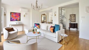 A modern living room with a white sofa, armchairs, a round coffee table, and a chandelier. - Incredibly Luxurious Bright 2 Bed with Balcony and Wow Eiffel View (Paris)