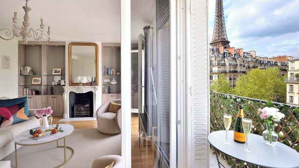 A modern living room with a fireplace, a dining area with a table and chairs, and a balcony with a view of the Eiffel Tower. - Incredibly Luxurious Bright 2 Bed with Balcony and Wow Eiffel View (Paris)