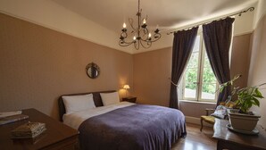 Quarto com cama grande, mesa de cabeceira, abajur, janela com cortinas e um vaso de planta.