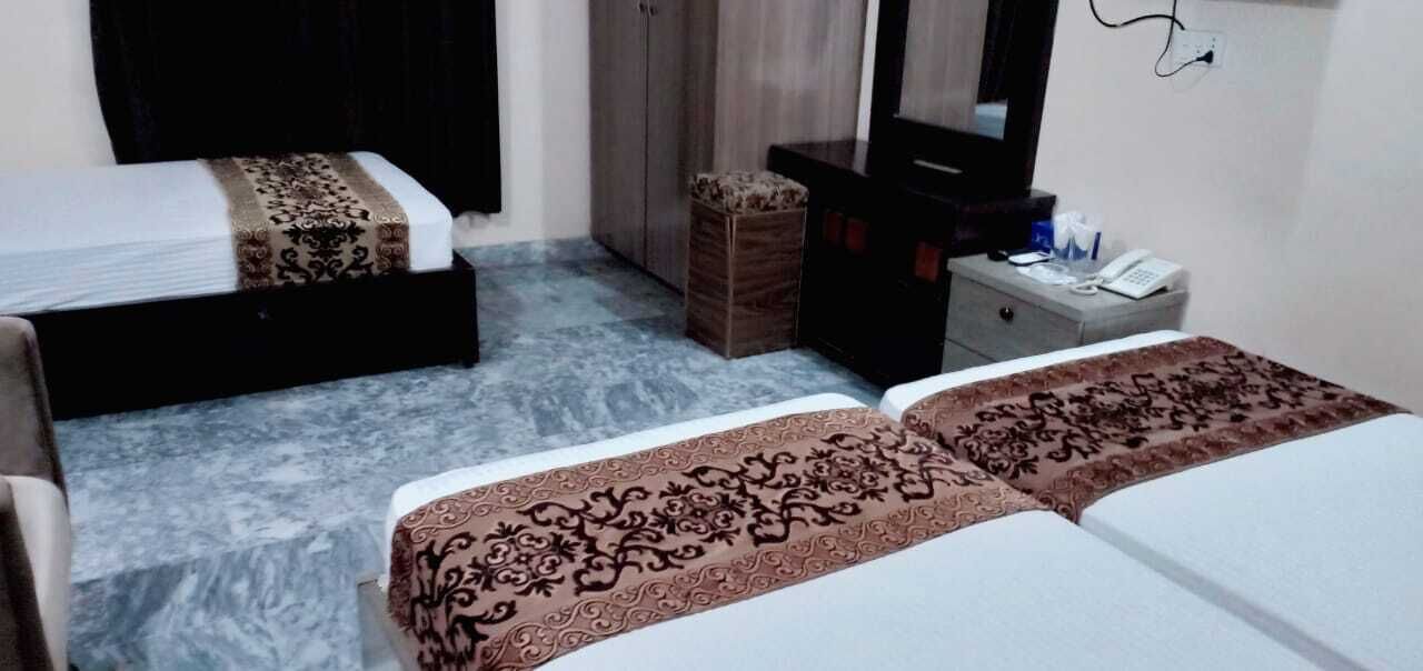 A hotel room with two beds, a wardrobe, a small cabinet, a desk with a telephone, and a mirror.