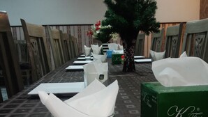 A dining table set with chairs, a glass with napkins, a K-Tissue box, and a small artificial tree. - Park view family hotel (Lahore)