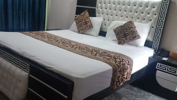 A neatly made bed with a patterned bedspread and pillows, a tufted headboard, and a bedside table with a lamp. - Park view family hotel (Lahore)