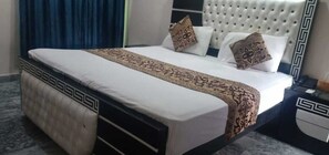A neatly made bed with a patterned bedspread and pillows, a tufted headboard, and a bedside table with a lamp. - Park view family hotel (Lahore)
