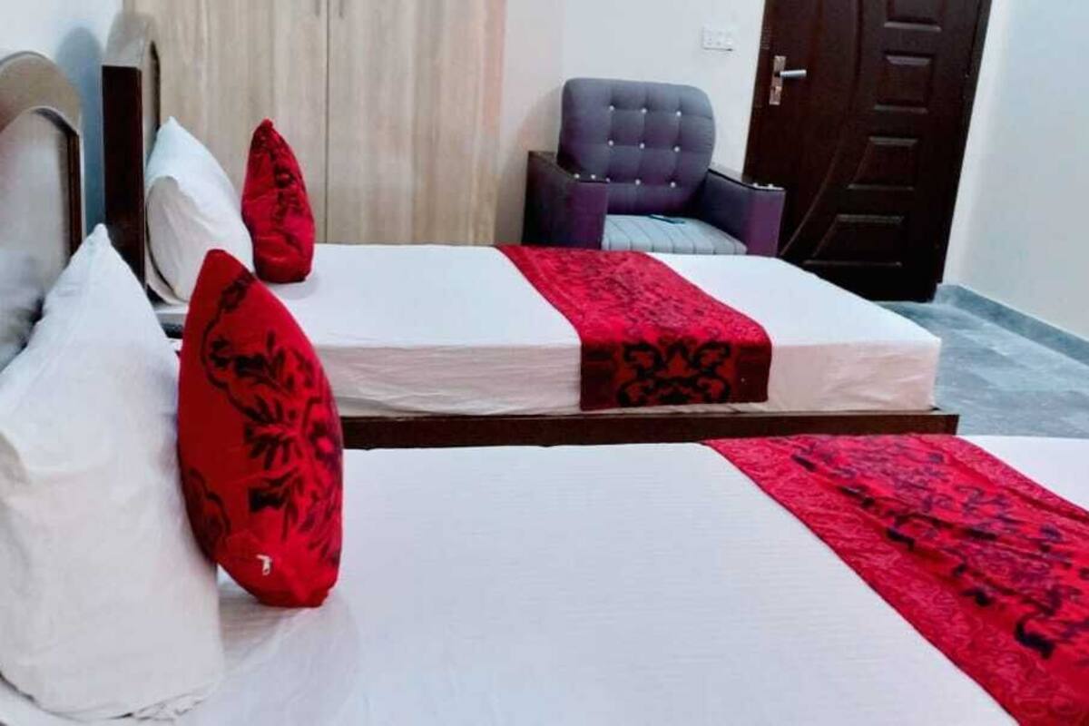 A hotel room with two beds, each with white linens and red decorative pillows. There is a chair and a door in the background.