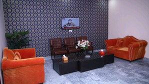 A room with patterned wallpaper, a television, two sofas, a coffee table, and a potted plant. - Park view family hotel (Lahore)