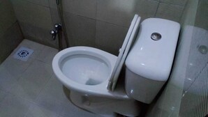 A standard toilet with a flush handle and a bidet attachment in a tiled bathroom. - Park view family hotel (Lahore)