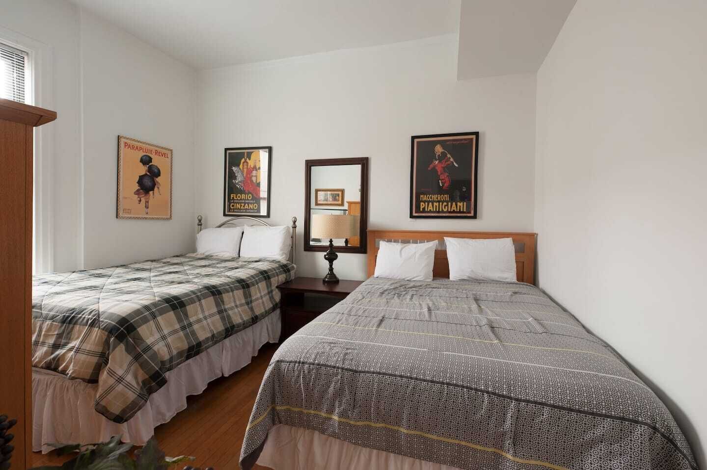 A bedroom with two beds, a nightstand with a lamp, and three posters on the wall.