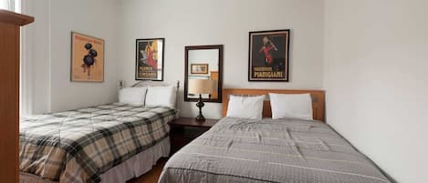 A bedroom with two beds, a nightstand with a lamp, and three posters on the wall.