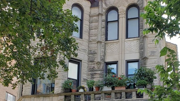 Un bâtiment en pierre doté de trois fenêtres en arc de cercle et d’un balcon orné de plantes en pot.