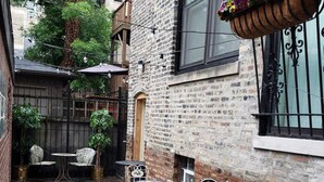 Une cour avec un mur en briques, une jardinière suspendue et un espace extérieur aménagé avec des chaises et des tables en métal.