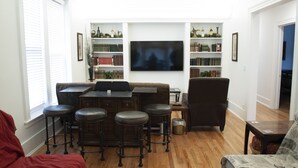 Un salon avec un plancher en bois, un canapé, une table basse, un téléviseur et des étagères à livres.