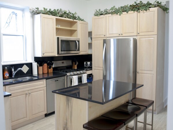 Una cocina moderna con armarios de madera clara, electrodomésticos de acero inoxidable y una isla central con taburetes de bar.