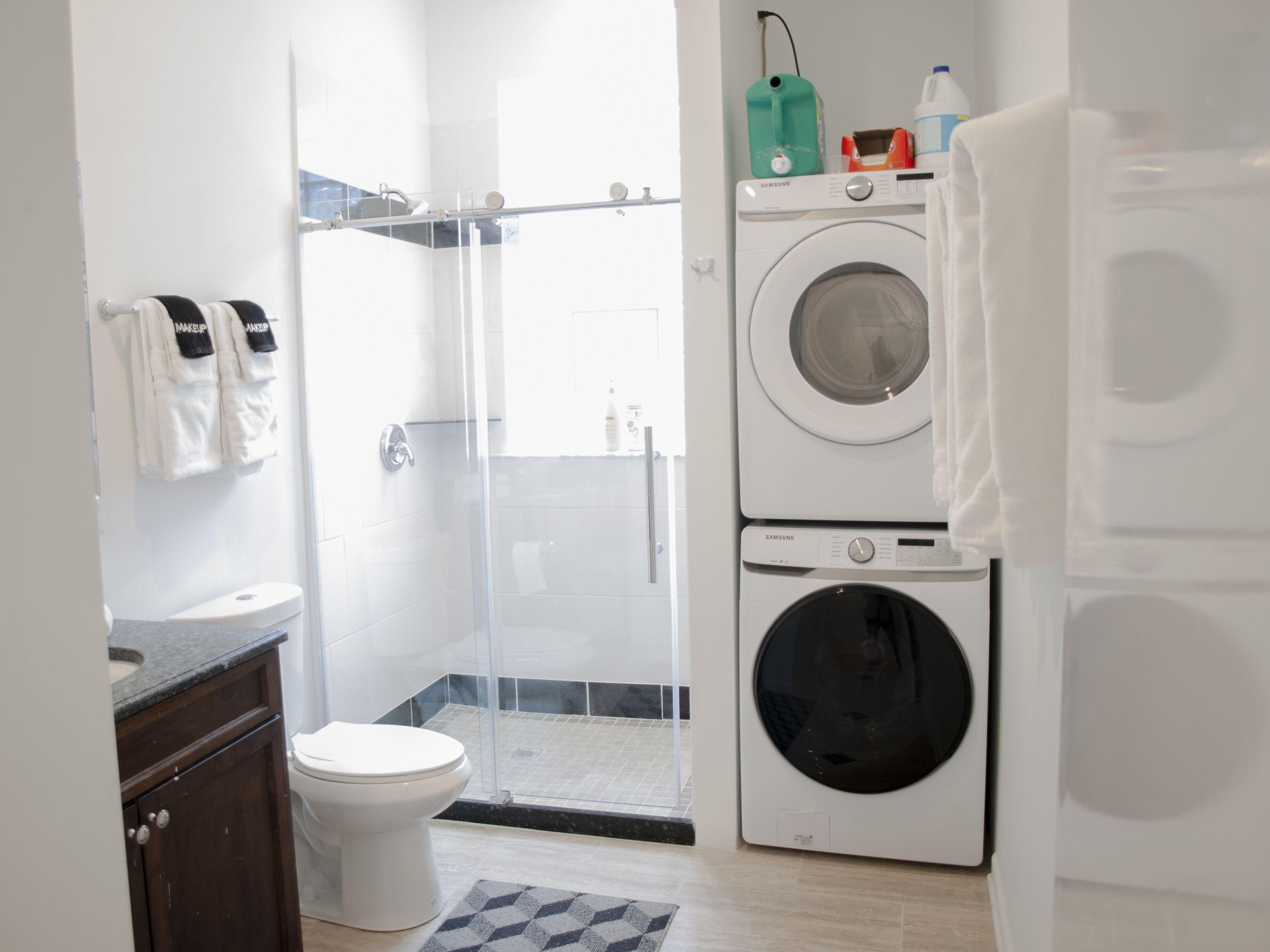 Un baño moderno con cabina de ducha de vidrio, inodoro blanco, lavadora y lavamanos con encimera oscura.