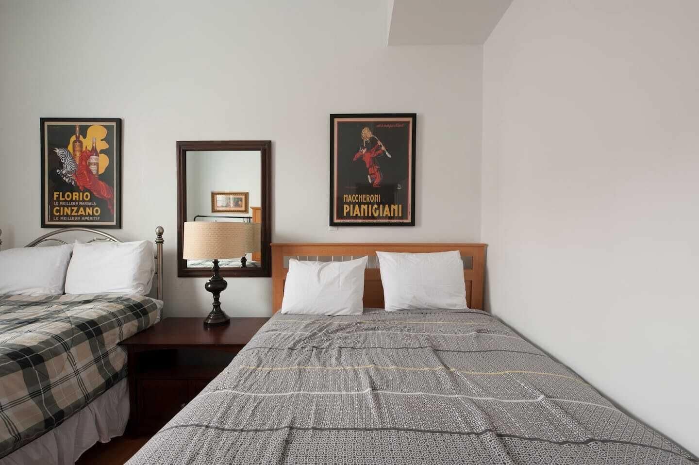 A hotel room with two beds, a nightstand with a lamp, and two framed posters on the wall.