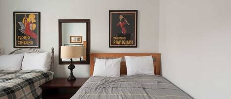 A hotel room with two beds, a nightstand with a lamp, and two framed posters on the wall.