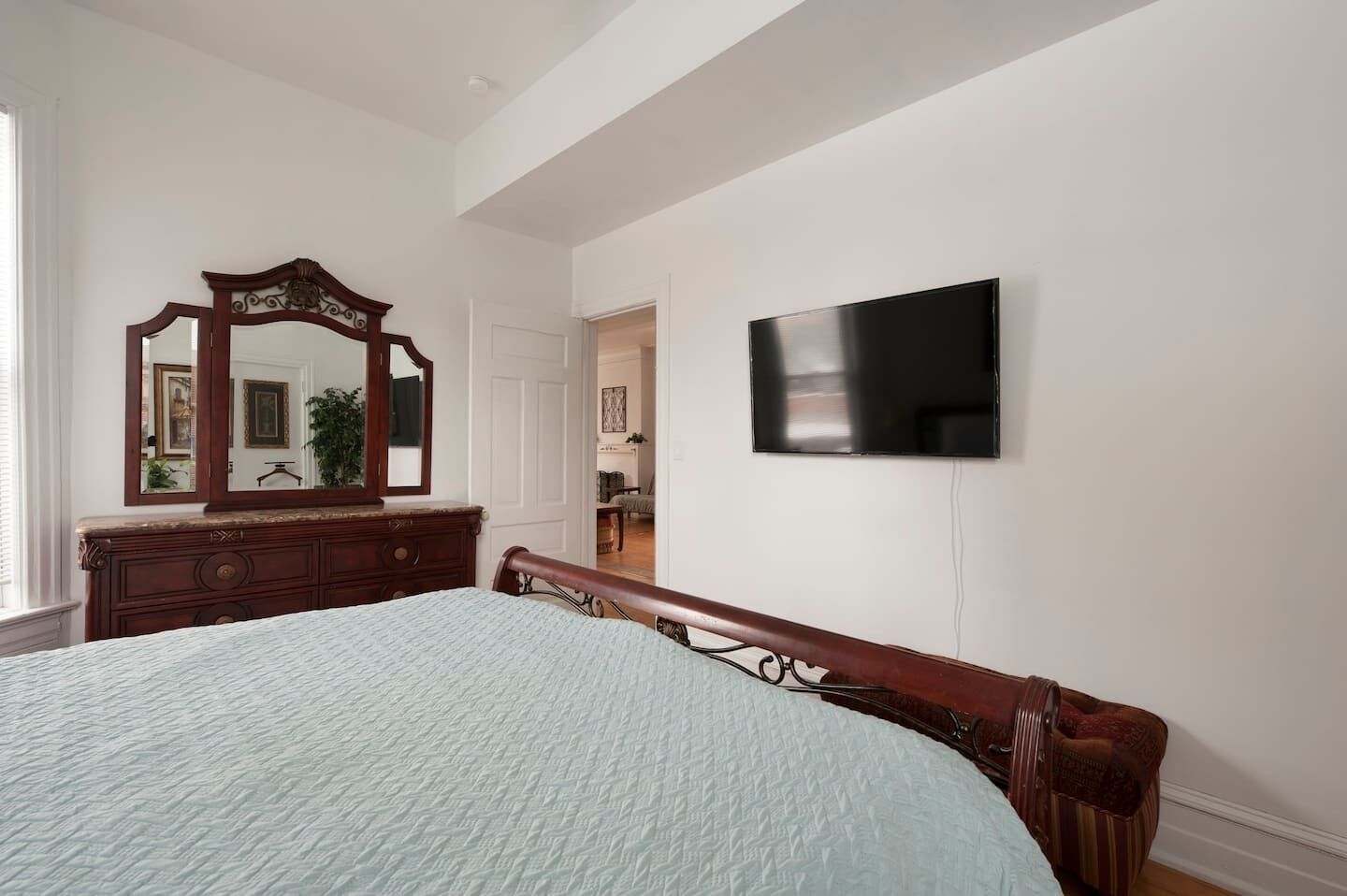 A bedroom with a bed, dresser, mirror, and TV.