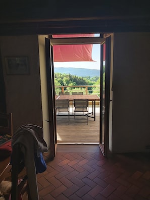 An open doorway leading to a deck with a table and chairs, overlooking a forested landscape.