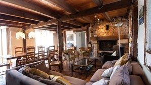 Un intérieur rustique agrémenté d’une cheminée en pierre, de poutres en bois et d’un coin salon confortable avec un canapé et des fauteuils.
