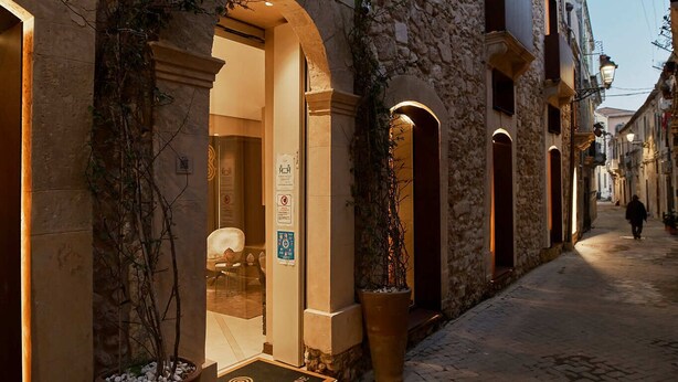 A stone building with arched doorways and a lit entrance. - Palazzo Salomone (Syracuse)
