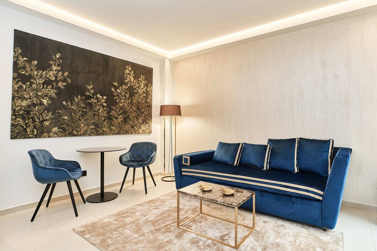 A modern living room with a blue sofa, two matching chairs, a round coffee table, and a large abstract painting on the wall.