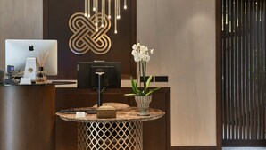 A modern reception desk with a laptop, a decorative wall piece, and a vase with white flowers. - Palazzo Salomone (Syracuse)