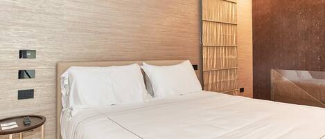 A modern hotel room with a large bed, a bedside table, and a wall-mounted control panel.
