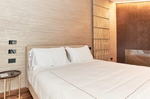 A modern hotel room with a large bed, a bedside table, and a wall-mounted control panel.