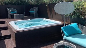 A hot tub on a wooden deck with two chairs and a table, surrounded by greenery and a clear sky. - Palazzo Salomone (Syracuse)