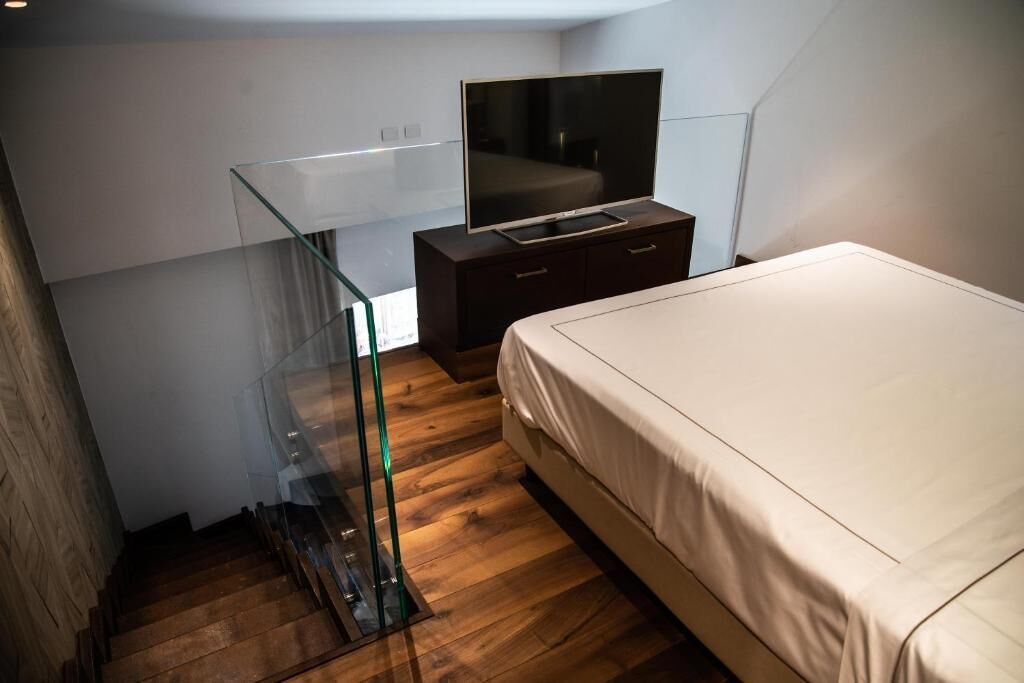 A bedroom with a bed, a TV on a dresser, and a glass railing.