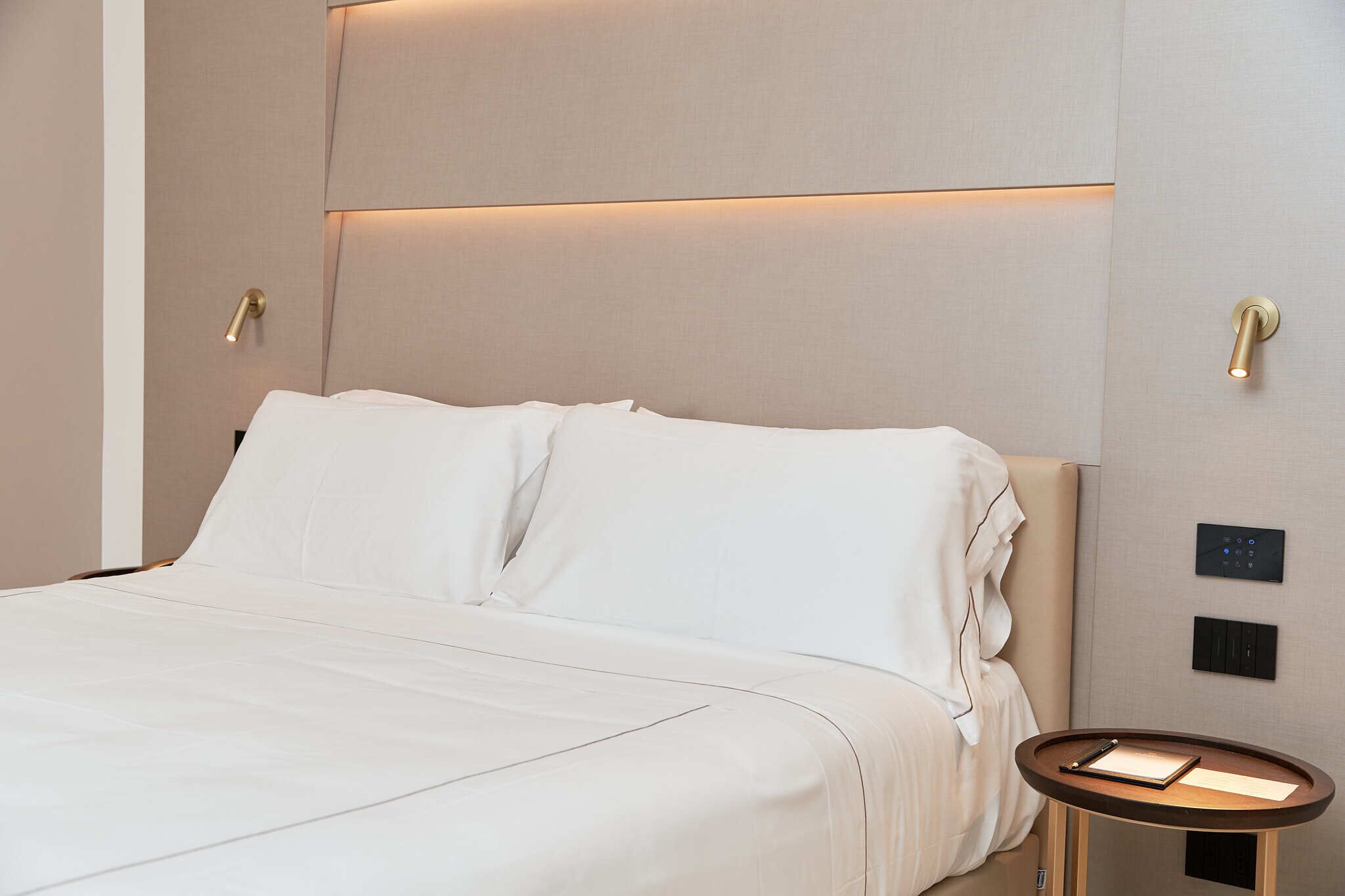 Una habitación de hotel con cama, mesita de noche y controles en la pared.