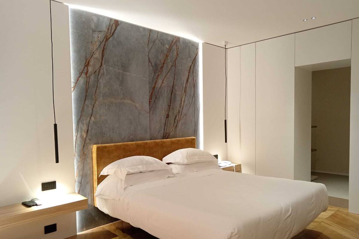 A modern bedroom with a large bed, wooden headboard, and a marble accent wall.