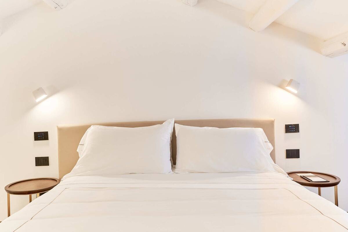 A neatly made bed with a headboard, two bedside tables, and wall-mounted light fixtures.