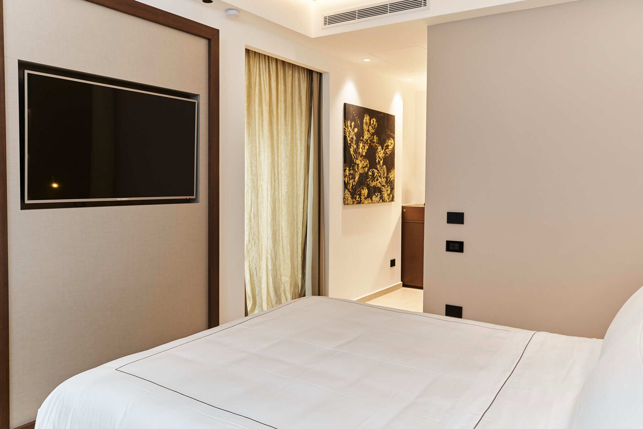 Ein Hotelzimmer mit einem großen Bett, einem wandmontierten Flachbildfernseher, einem Gemälde und einer Tür zu einem Badezimmer.