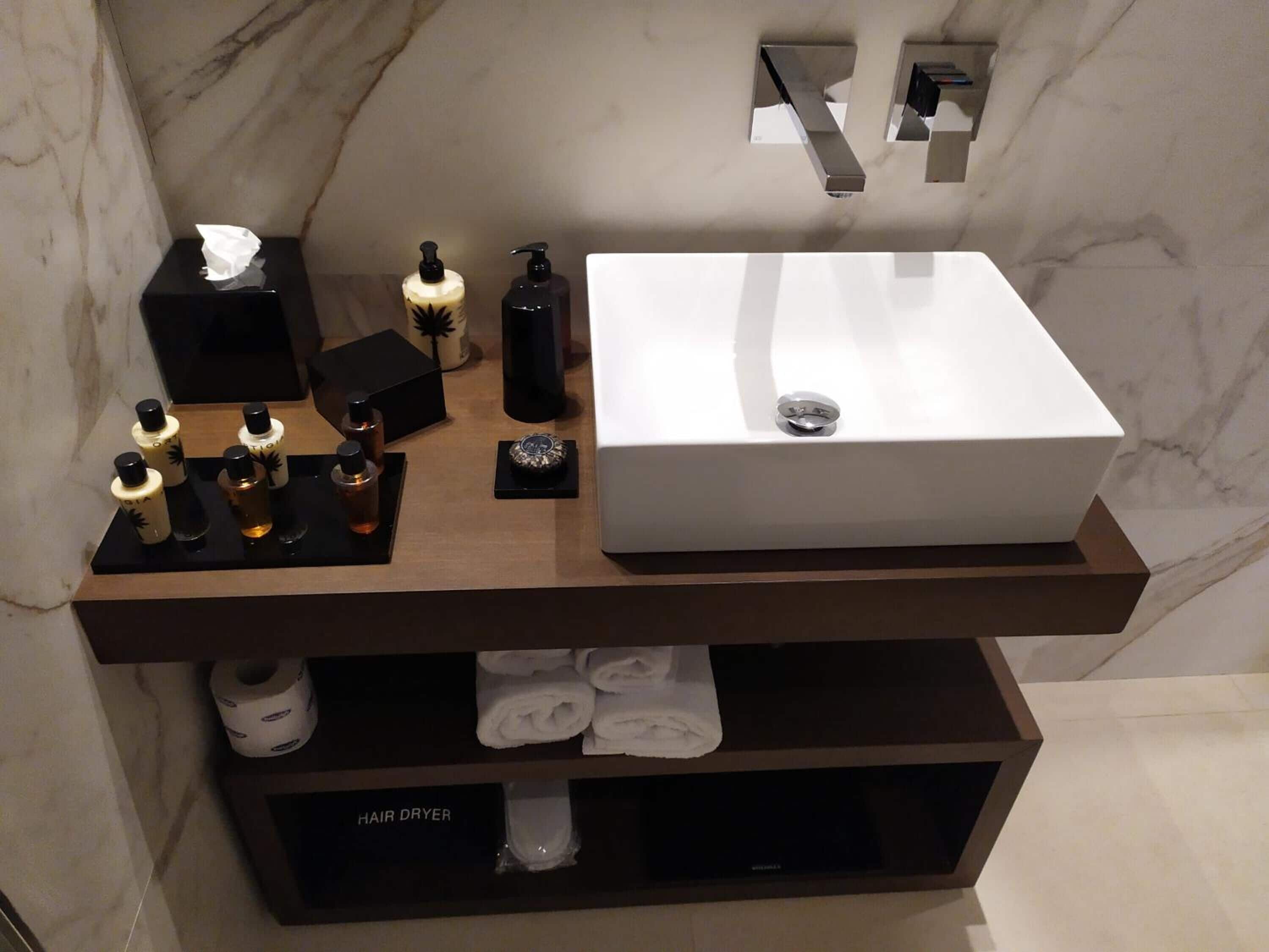 Un mueble de baño con lavamanos blanco, dispensadores de jabón negros, una caja de pañuelos y un secador de pelo.