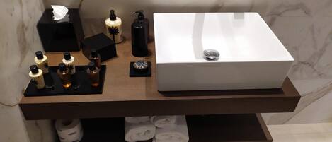 Un meuble-lavabo de salle de bain avec un lavabo blanc, des distributeurs de savon noirs, une boîte à mouchoirs et un sèche-cheveux.