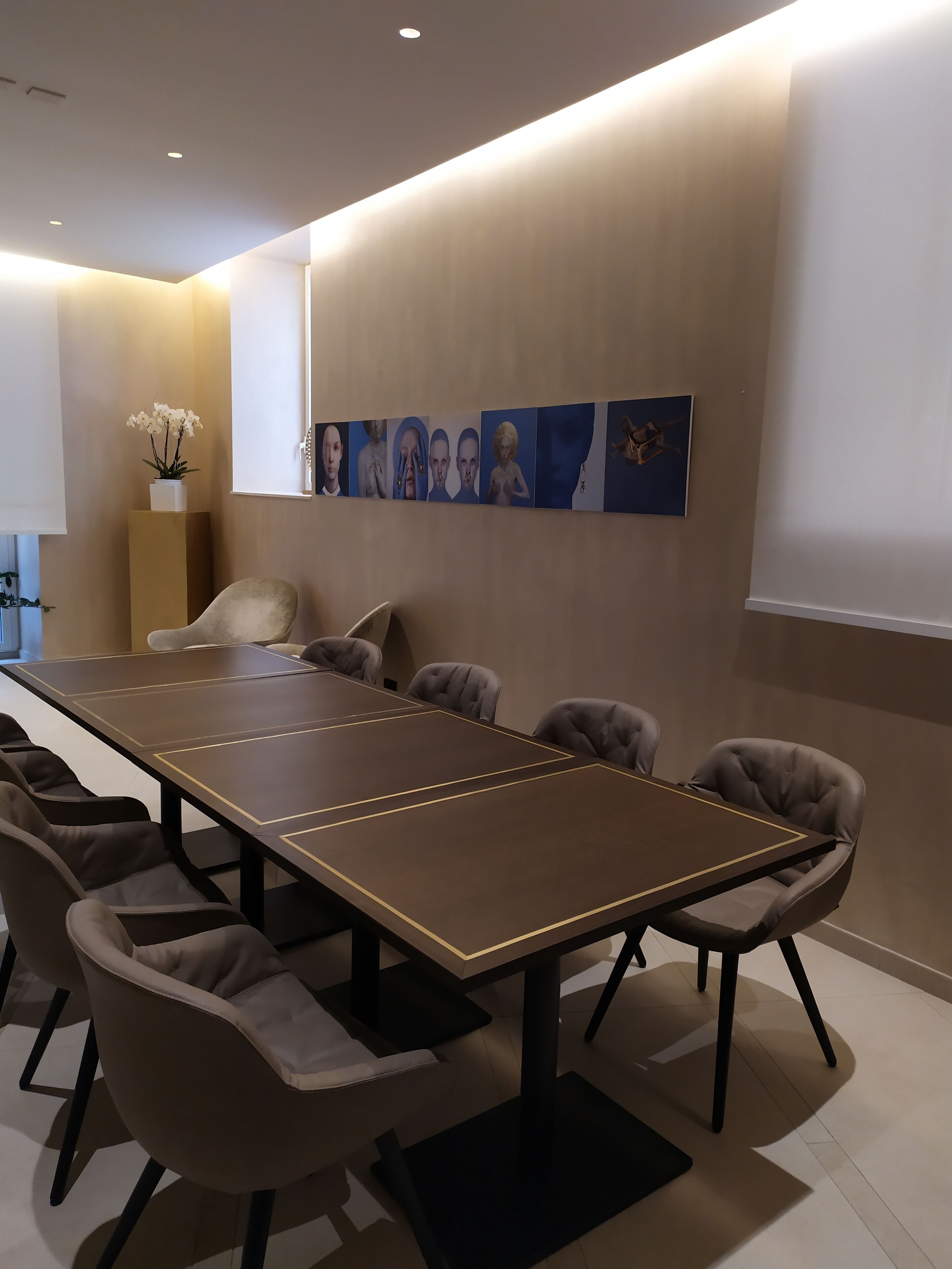 Un salón de conferencias con una larga mesa y ocho sillas, una planta en maceta y varias obras de arte en la pared.