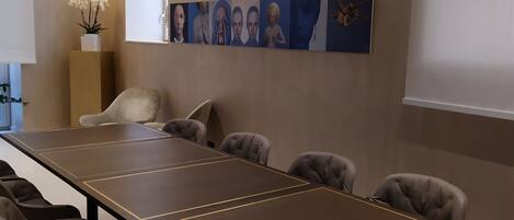 Un salón de conferencias con una larga mesa y ocho sillas, una planta en maceta y varias obras de arte en la pared.